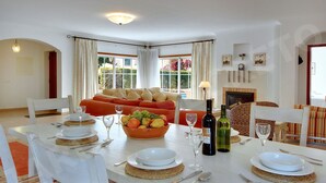A dining area with a white table set for four, a fruit bowl, and a fireplace.