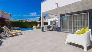 A modern outdoor patio with a pool, white lounge chairs, and a dining area.