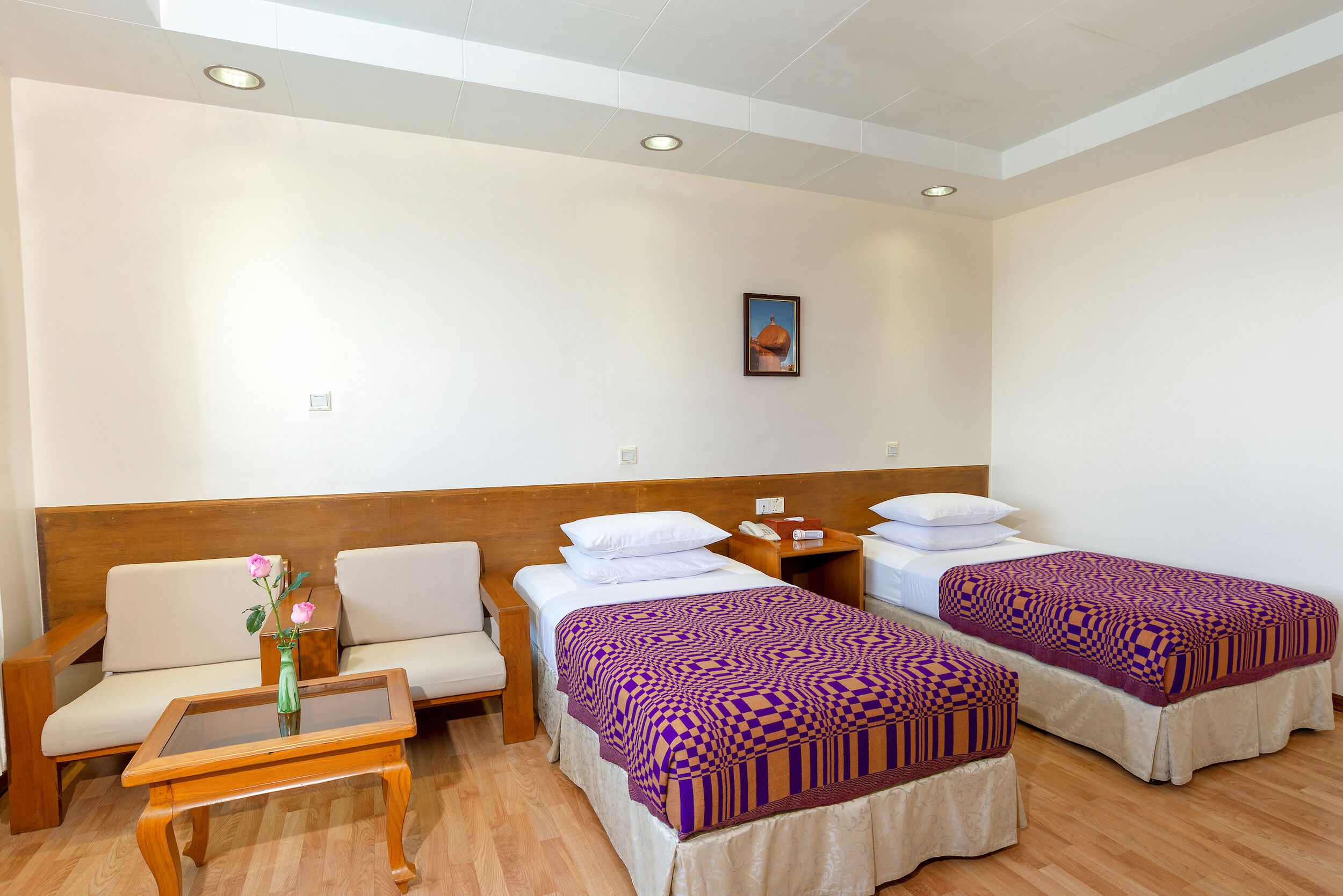 A hotel room with two beds, a sofa, a small table, and a vase with flowers.