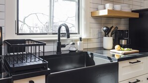 A kitchen with a black sink, wooden shelves, and a window with a view of bare trees. - The Russell House - Walk to Restaurants & Bars! (Nashville)