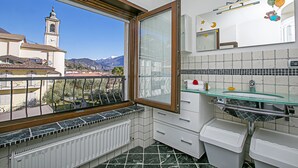Un baño con vista a una iglesia y montañas, cabina de ducha de vidrio y suelo de baldosas.