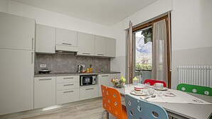 A modern kitchen with white cabinets, a microwave, and a dining area with a table and chairs. - Bella Arco Apartment with Balcony, Arco, Italy (Arco)
