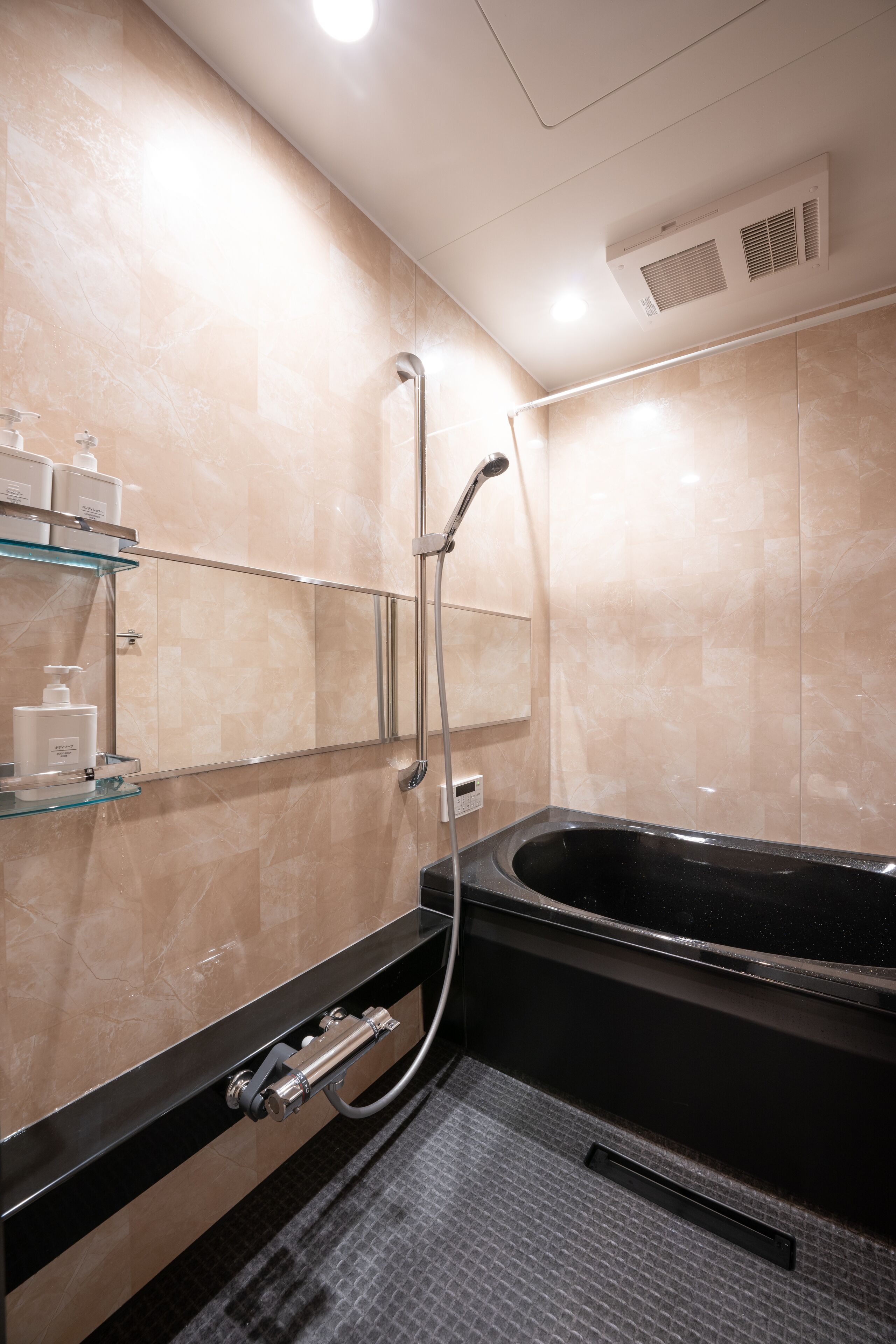 A modern bathroom with a black bathtub, a glass shelf with toiletries, and a handheld showerhead.