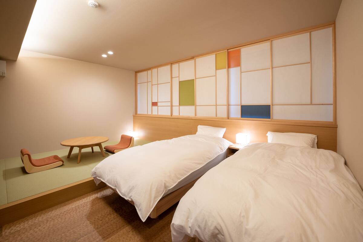 A hotel room with two beds, a small table, and a chair.