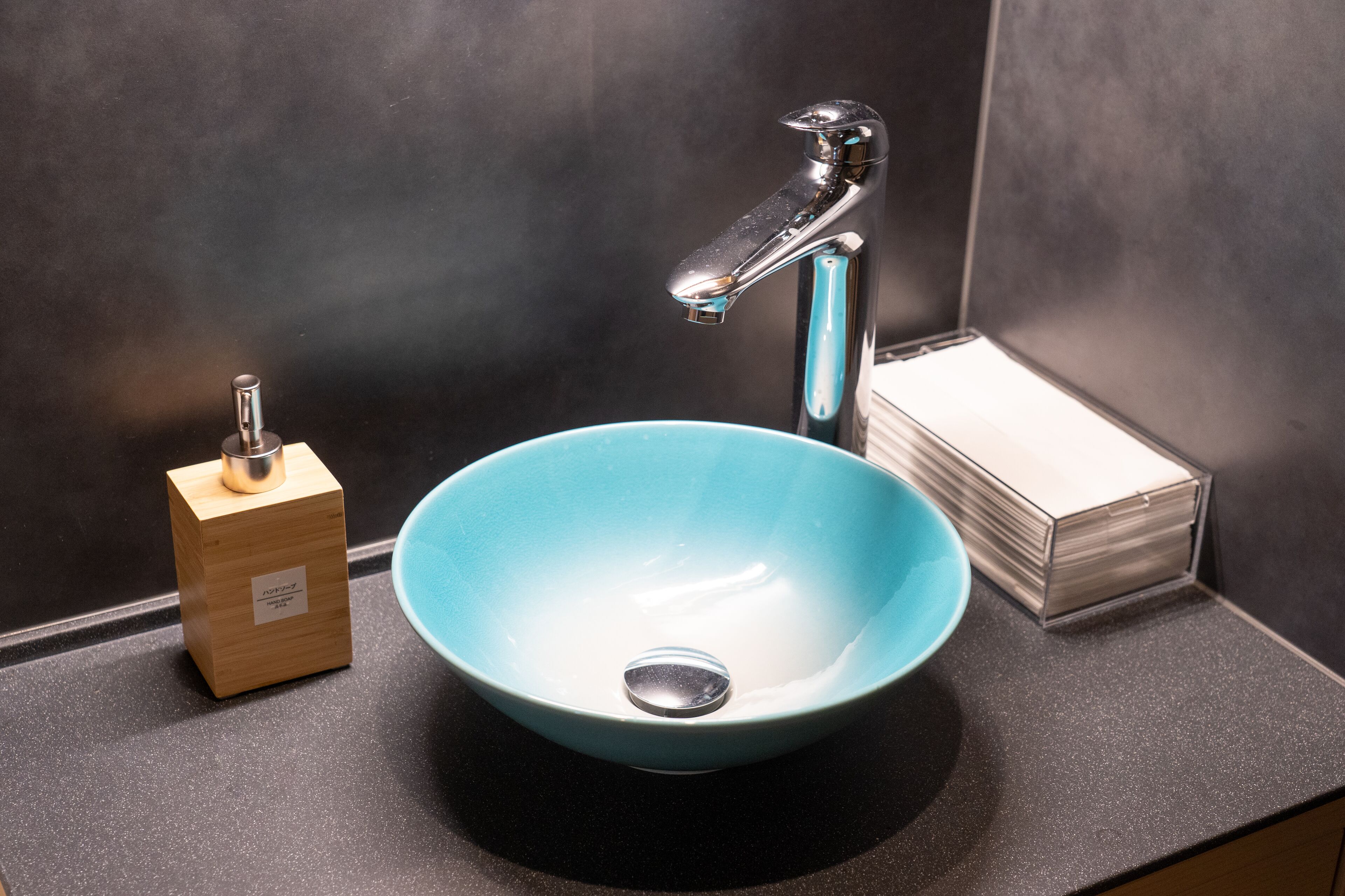 Un lavabo de salle de bain avec un receveur bleu, un robinet chromé et un distributeur de savon en bois.