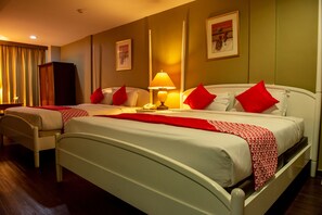 A hotel room with two beds, each with white bedding and red pillows, a bedside table with a lamp, and a wardrobe.