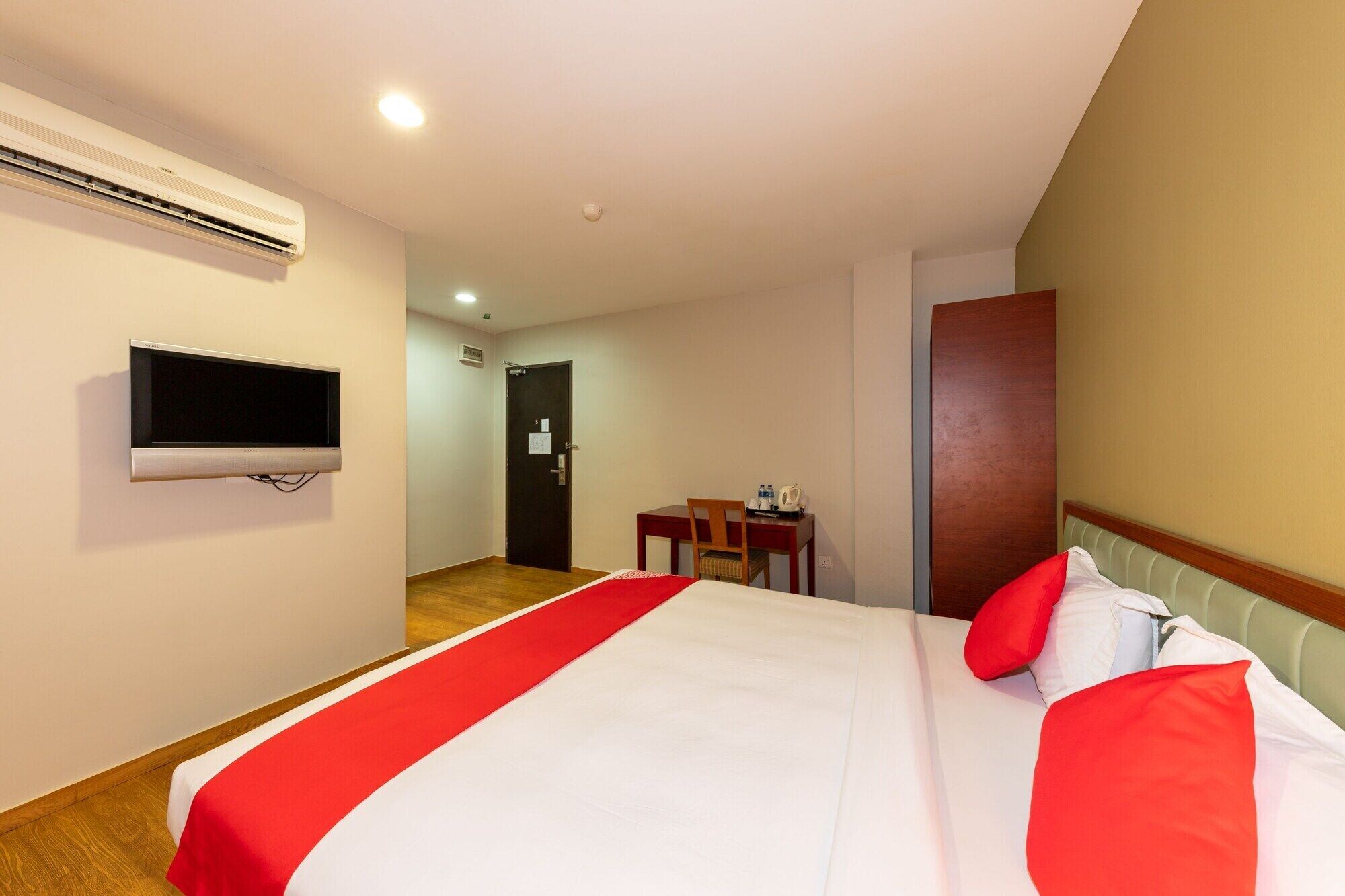 A hotel room with a bed, a TV mounted on the wall, a desk with a chair, and a door leading to another room.