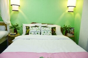 Ein ordentlich bezogenes Bett mit einer weiß-rosa Tagesdecke, zwei Nachttische mit Lampen und grüne Wände.