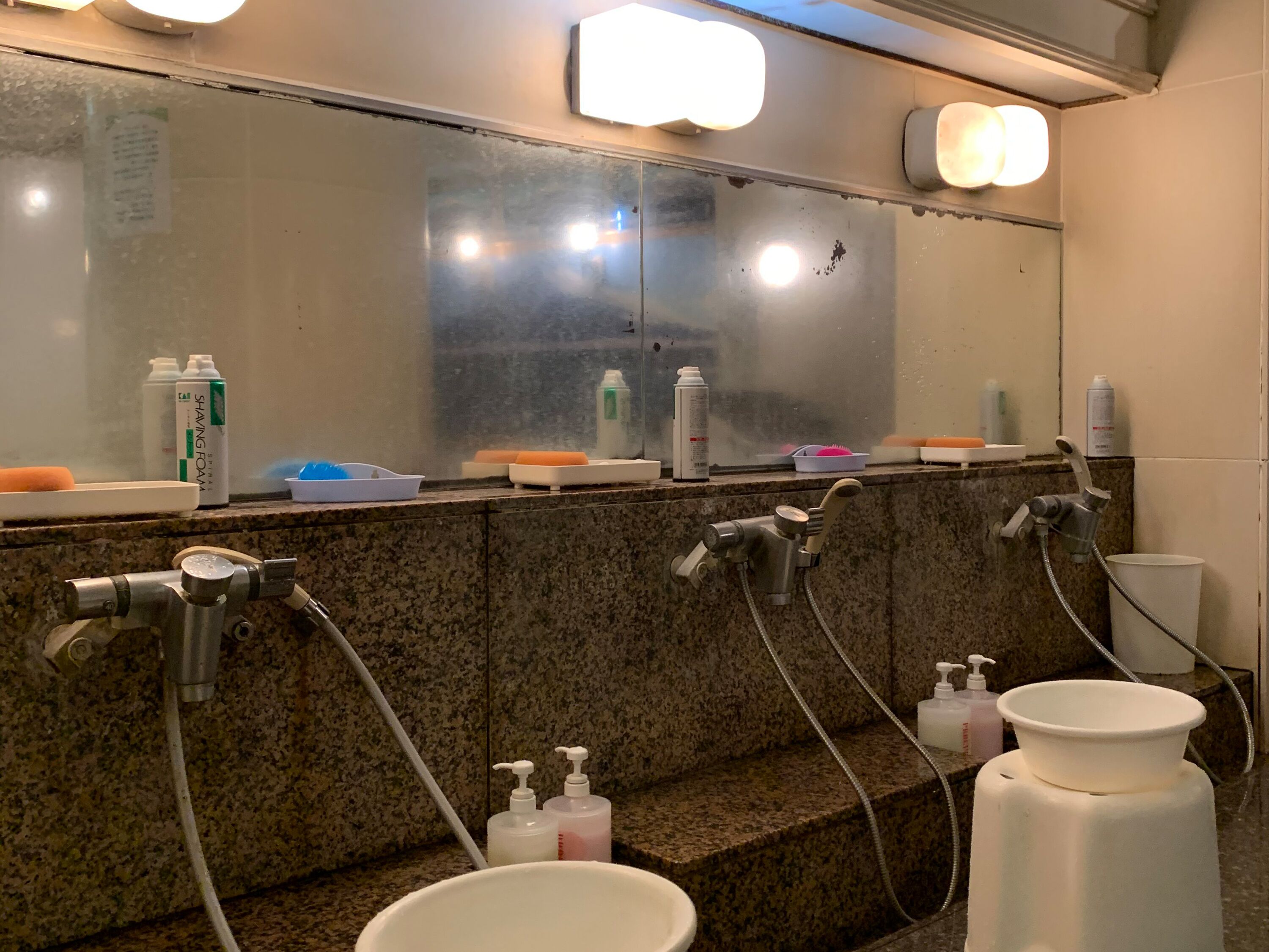 A public restroom with multiple sinks, a mirror, and various toiletries.