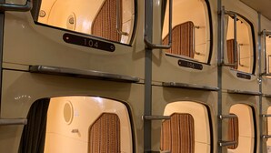A row of bunk beds with individual numbers, metal railings, and a patterned headboard. - Funabashi Grand Sauna and Capsule Hotel - Caters to Men (Funabashi)