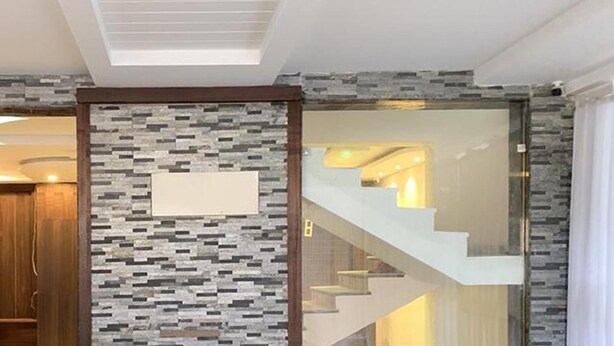 Un interior moderno con una pared de diseño de piedra, una puerta de madera y una escalera que lleva a un nivel superior iluminado.