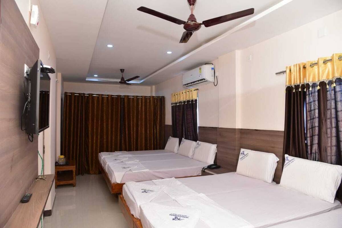 A hotel room with three single beds, a TV mounted on the wall, a ceiling fan, and an air conditioning unit.