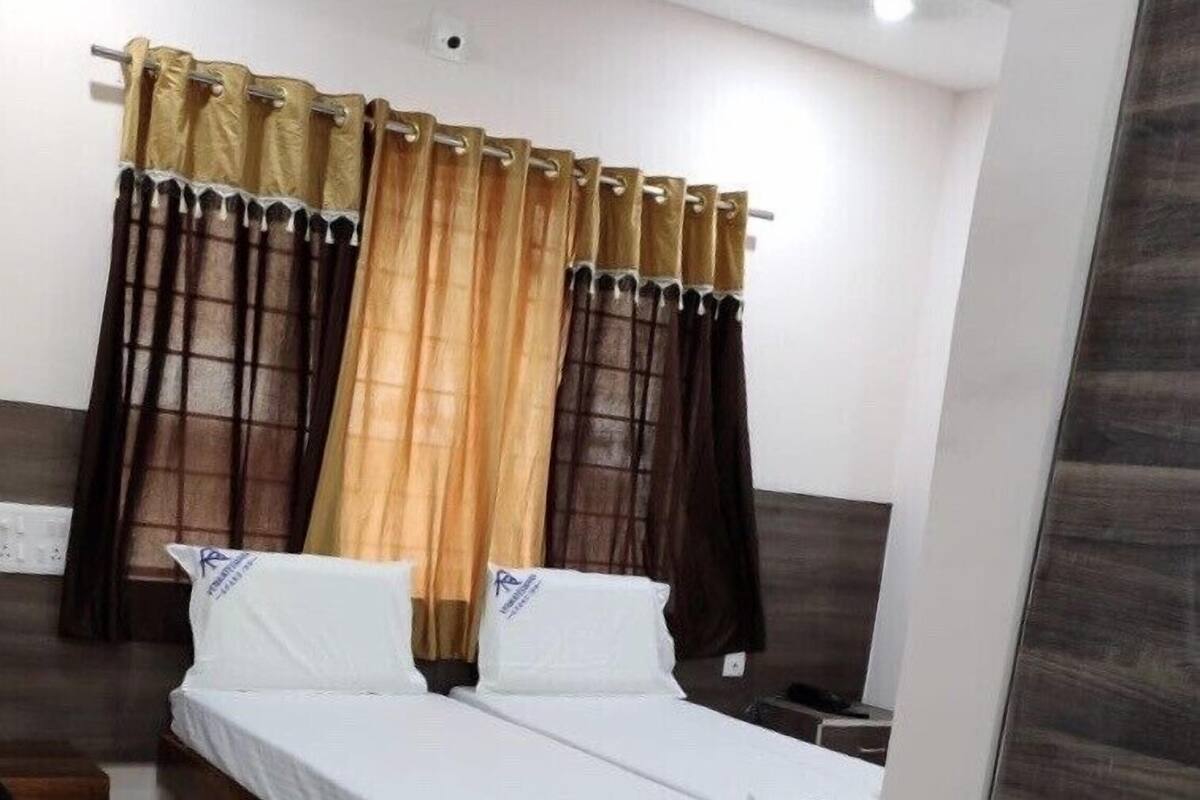 A hotel room with a bed, two pillows, and a curtain with a gold and brown pattern.