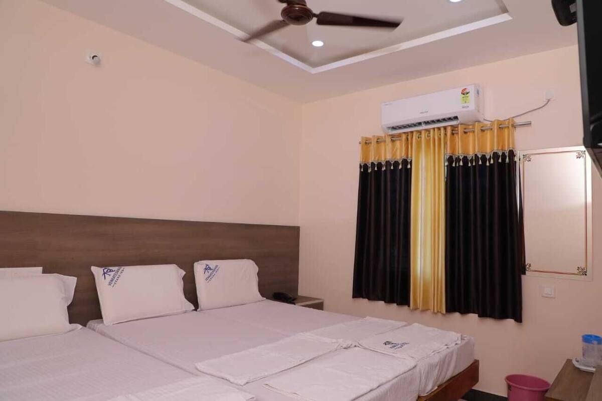 A hotel room with a bed, a ceiling fan, an air conditioning unit, and curtains.