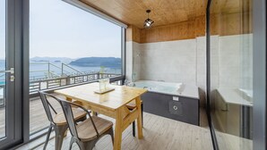 A modern bathroom with a bathtub, shower, and large windows offering a view of the sea. - Yeosu Sunset Hostel and Pension (Yeosu)
