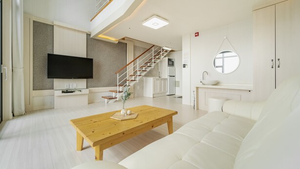 A modern living room with a flat-screen TV, a wooden coffee table, a white sofa, and a staircase leading to a kitchen. - Yeosu Sunset Hostel and Pension (Yeosu)