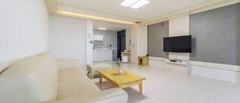A modern living room with a sofa, a wooden coffee table, and a flat-screen TV mounted on the wall.