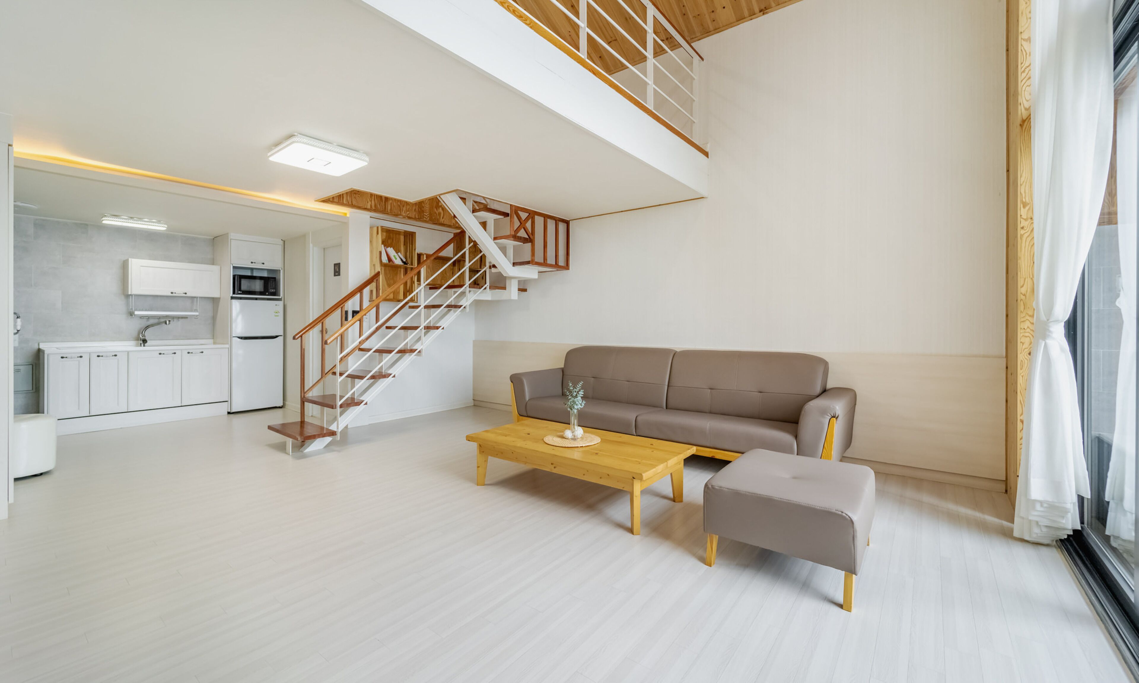 Amplia sala de estar con escalera de madera, un sofá, una mesa de centro y una cocina al fondo.