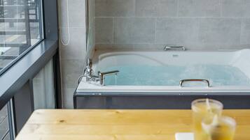 Un baño moderno con bañera, una ventana y una mesita de madera con un vaso de agua.