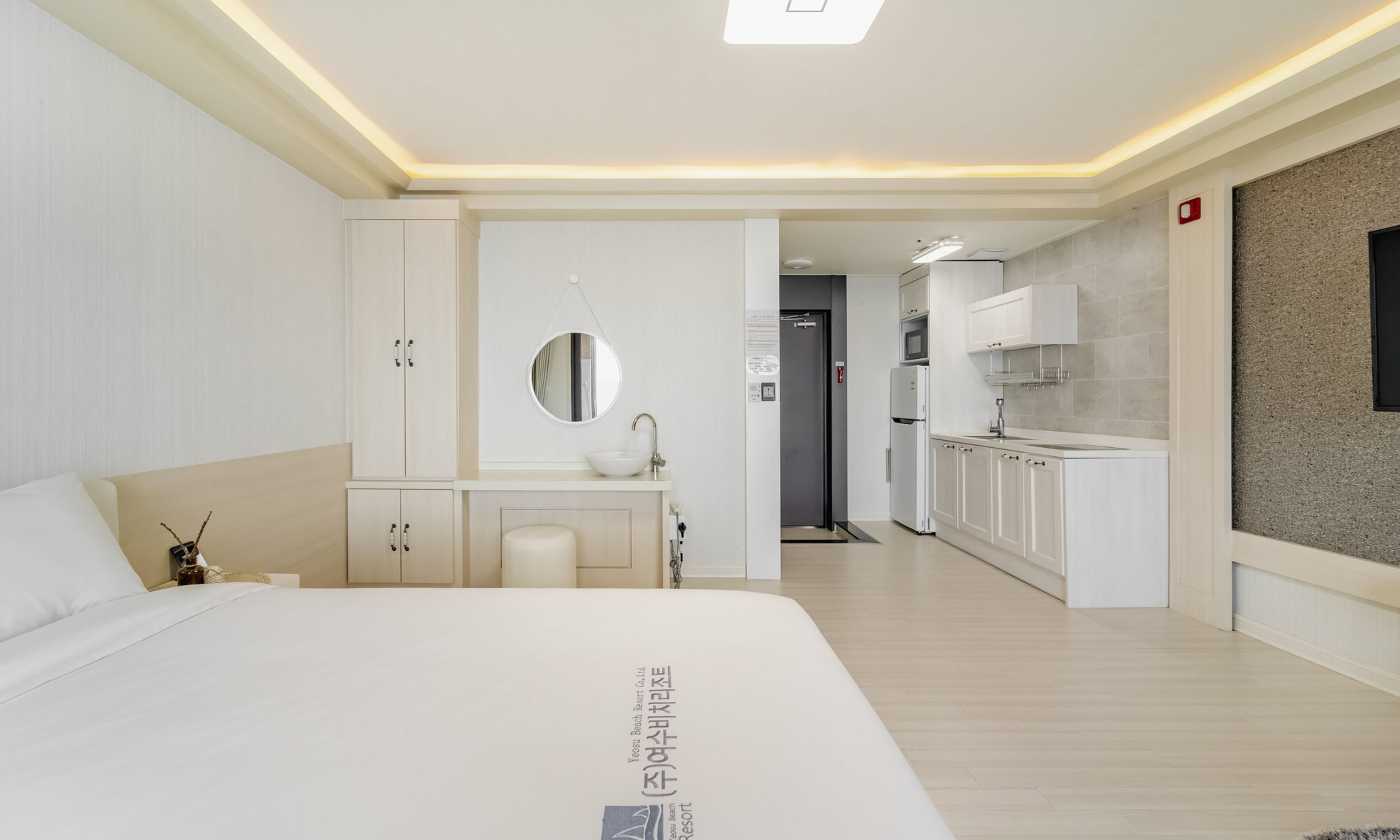 A modern hotel room with a large bed, a vanity with a mirror, a small kitchenette, and a bathroom.