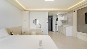 A modern hotel room with a large bed, a vanity with a mirror, a small kitchenette, and a bathroom.