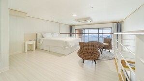 A modern bedroom with a large bed, a bedside table, two wicker chairs, and a view of the sea through a large window. - Yeosu Sunset Hostel and Pension (Yeosu)