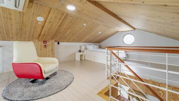 Ein modernes Schlafzimmer im Loft-Stil mit schrägem Dach, einem roten und weißen Stuhl, einem weißen Bett und einer Holztreppe.
