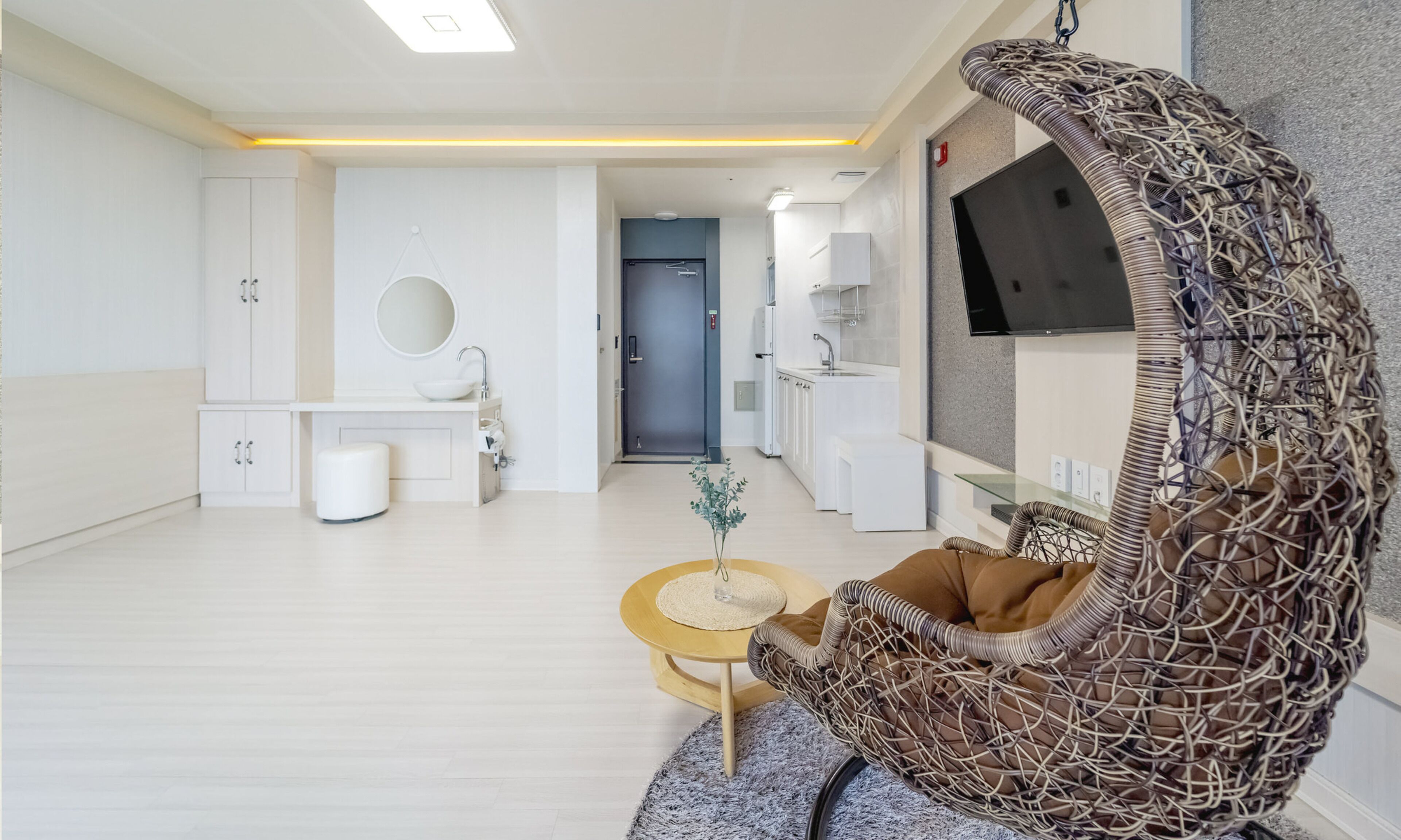A modern living room with a wicker chair, a round coffee table, and a TV mounted on the wall.