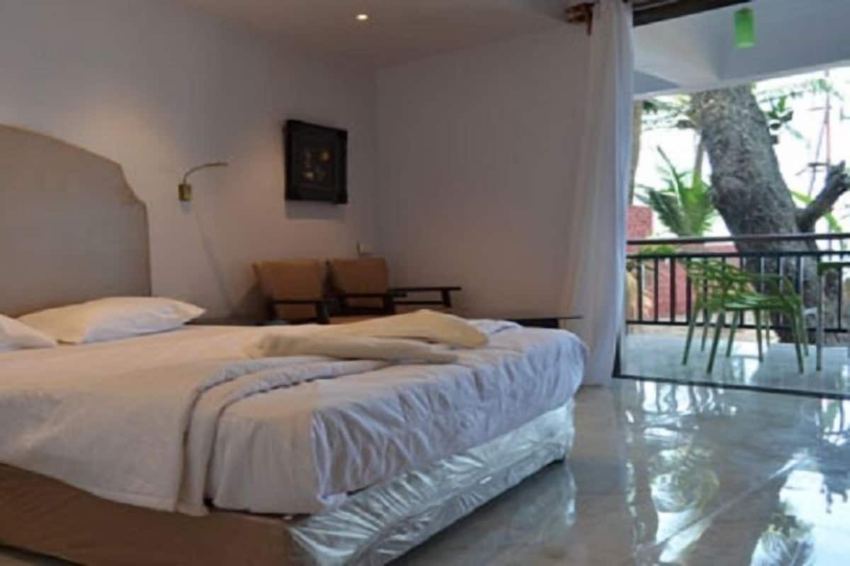 Ein Hotelzimmer mit einem großen Bett, einem kleinen Tisch, einem Stuhl und einem Balkon mit Blick auf Bäume.