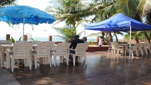 Zona de estar al aire libre con sillas de plástico blanco y una sombrilla azul, con vista a la playa.