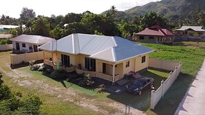 A two-story house with a sloped roof, a porch, and a fenced yard. - My Ozi Perl Self Catering Guest House (Praslin Island)