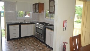 A kitchen with a gas stove, oven, and sink, wooden cabinets, and patterned flooring. - My Ozi Perl Self Catering Guest House (Praslin Island)