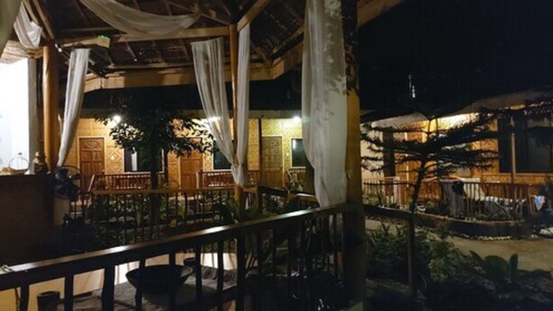 An outdoor seating area with tables and chairs, a wooden pergola, and a view of the surrounding landscape. - Oslob New Village by Cocotel (Oslob)