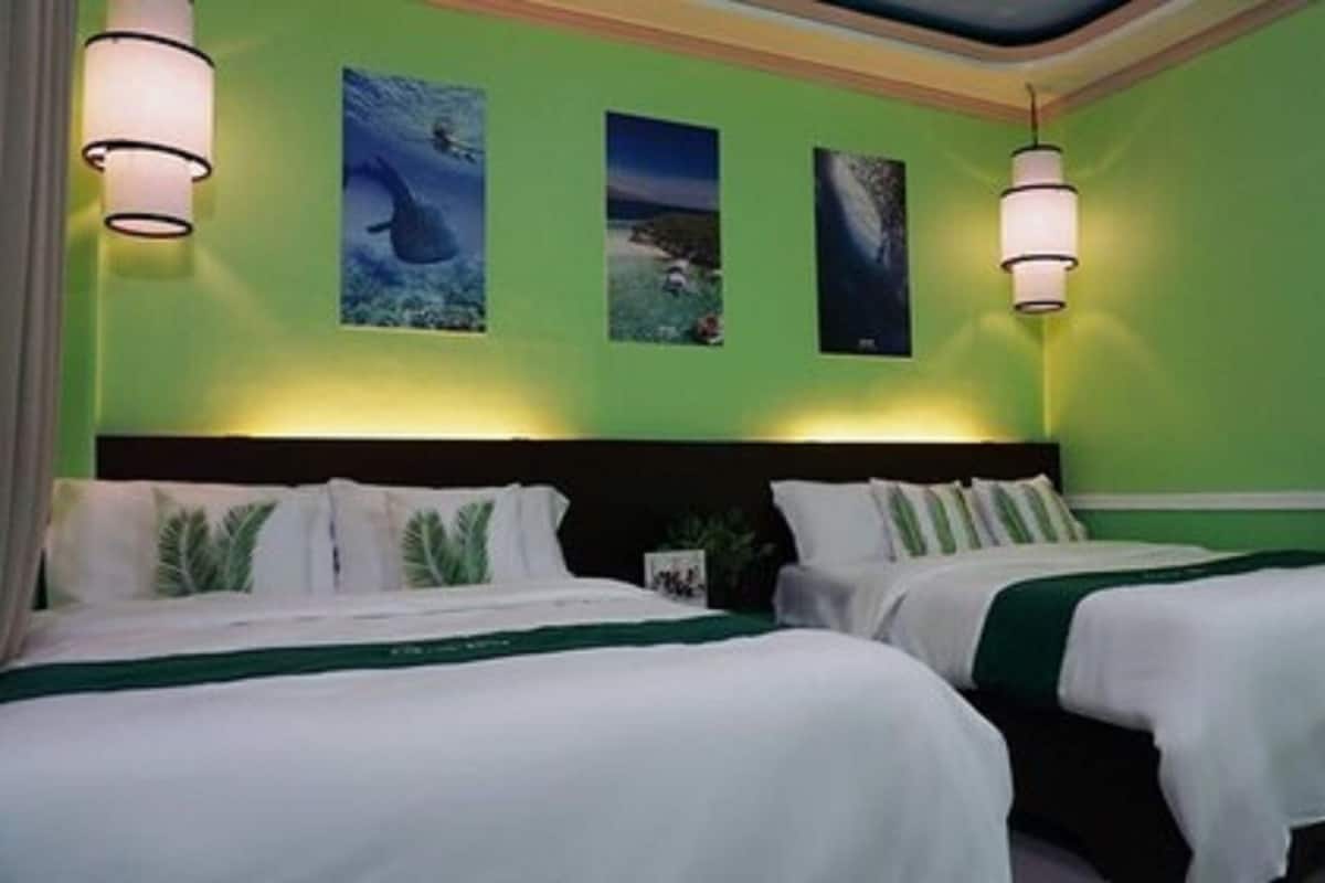 Une chambre d’hôtel avec deux lits, un mur vert et trois tableaux encadrés.