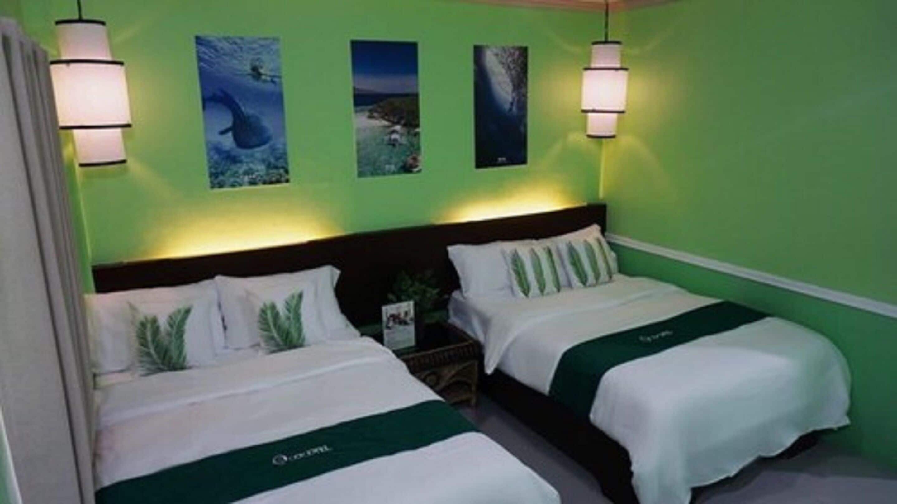 A hotel room with two beds, green walls, and three framed pictures on the wall.
