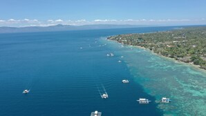 An aerial view of a coastal area with clear blue waters, boats, and a densely vegetated shoreline. - Oslob New Village by Cocotel (Oslob)