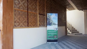 Une affiche promotionnelle pour COCOTEL BUREAU, placée devant un bâtiment doté d’un mur en bambou tressé et d’un escalier.