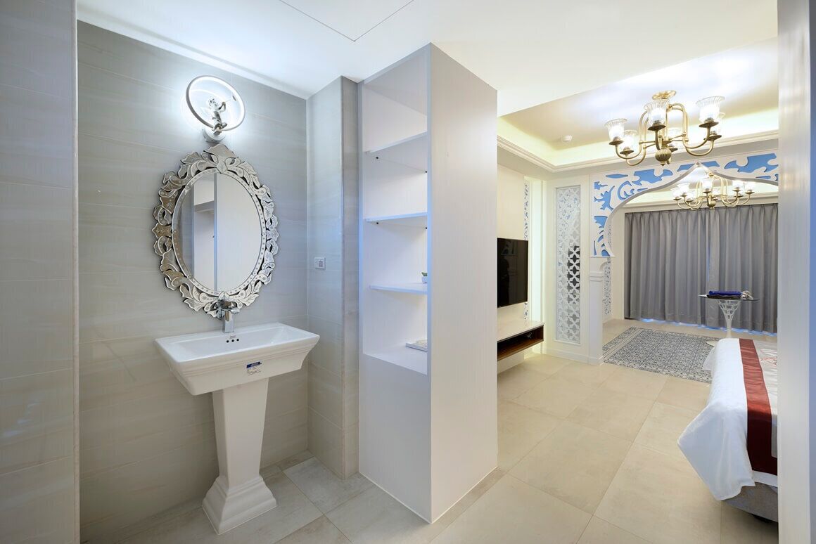 A modern bathroom with a pedestal sink, a decorative mirror, and a vanity with shelves.