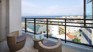 A balcony with wicker furniture, a glass railing, and a view of the city and sea. - Hand in Hand INN (Liuqiu)