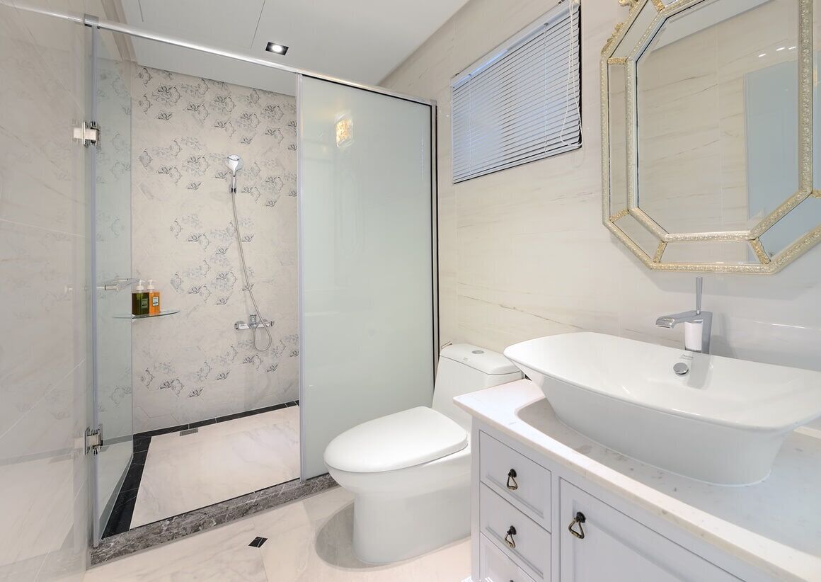 A modern bathroom with a glass-enclosed shower, a white toilet, and a vanity with a large sink and mirror.