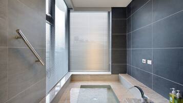 Un baño moderno con bañera de hidromasaje acristalada, barra de apoyo y un amplio ventanal con persianas.