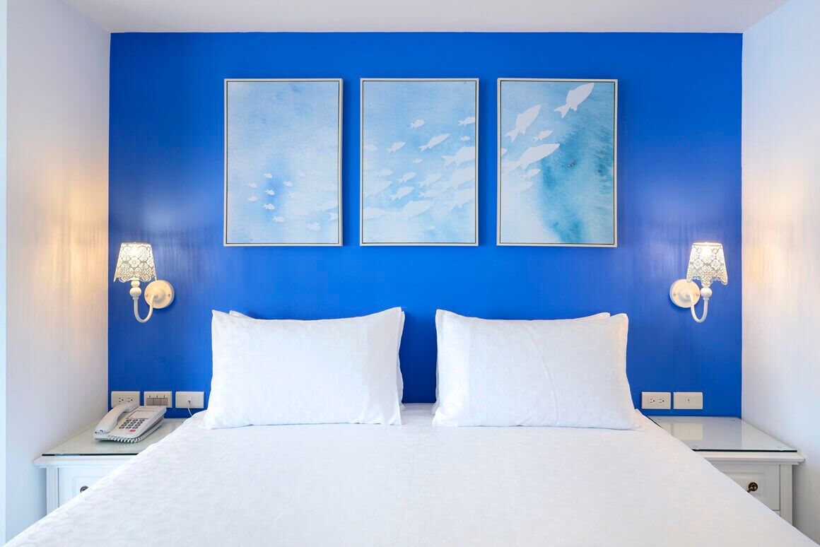 A hotel room with a blue accent wall, a bed with white bedding, two bedside tables, and wall-mounted lamps.