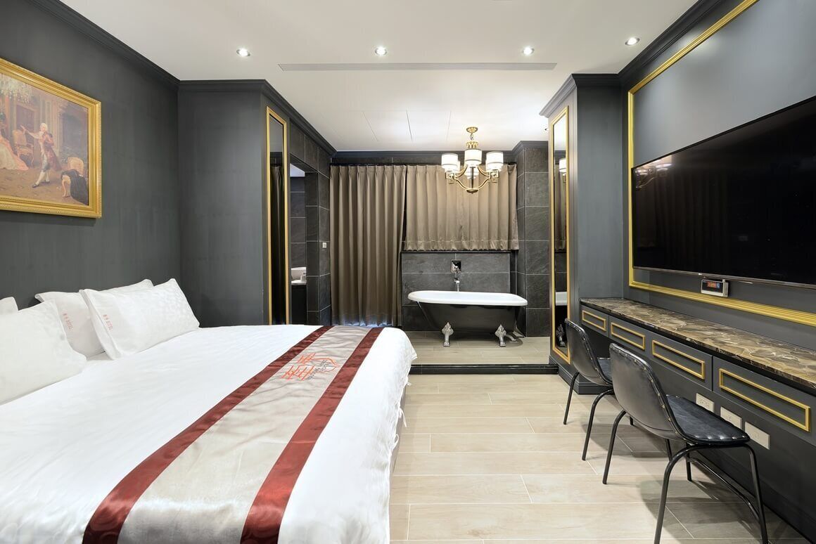 A modern hotel room with a large bed, a vanity with a mirror, a bathtub, and a TV.