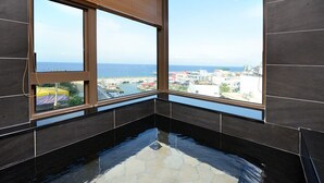 A room with large windows, a tiled floor, and a view of the sea and buildings. - Hand in Hand INN (Liuqiu)