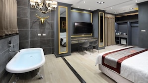 A modern hotel room with a bathtub, a large bed, a TV, and a desk with chairs. - Hand in Hand INN (Liuqiu)