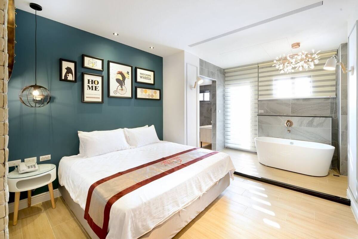 Un dormitorio moderno con una cama grande, una mesita de noche, un televisor en la pared y un baño con bañera.