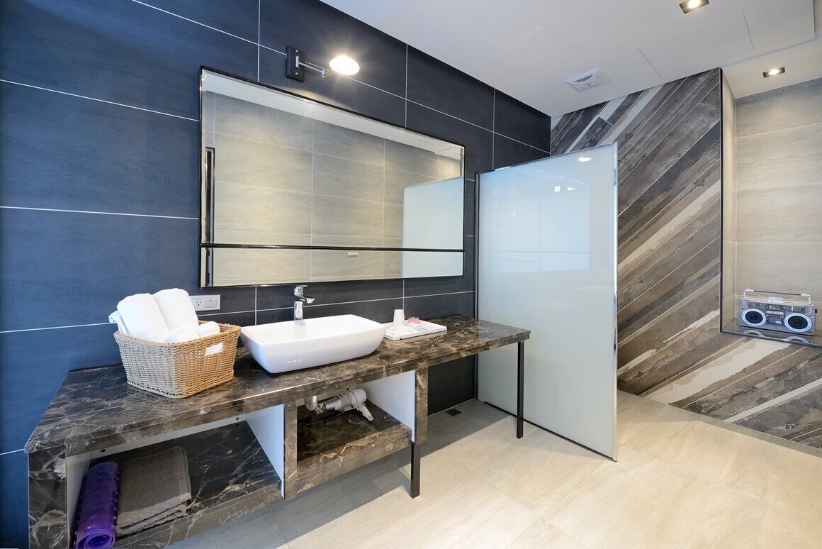 Un bagno moderno con uno specchio grande, un lavandino bianco, un piano di lavoro in marmo e una zona doccia.