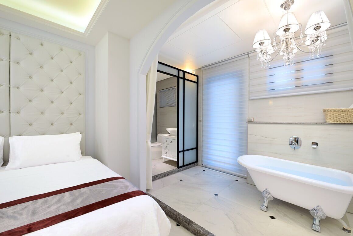 Une chambre à coucher moderne avec un grand lit, une baignoire sur pieds de style classique et une salle de bain séparée, visible à travers une porte coulissante.
