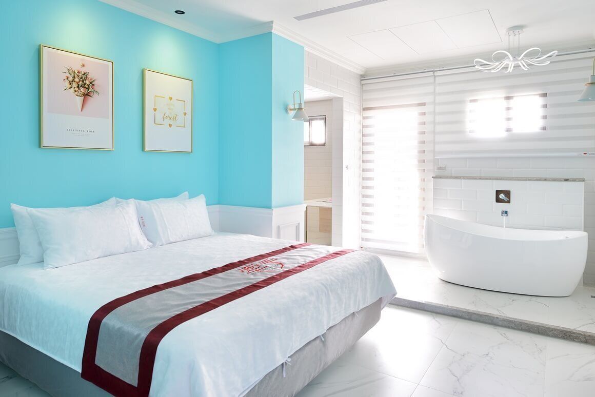 A modern bedroom with a large bed, a white bathtub, and a bright blue accent wall.