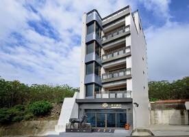 Un edificio moderno de varios pisos, una entrada destacada con una estatua y un cielo despejado.